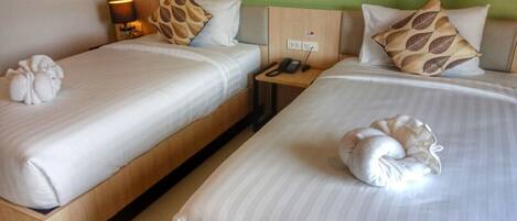 A hotel room with two beds, each with a pillow and a decorative item. There is a nightstand with a phone and a lamp between the beds.