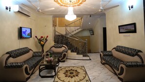 A living room with a chandelier, two sofas, a coffee table, and a TV. - Novem Inn & Holidays (Sylhet)