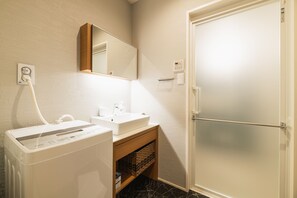 A bathroom with a white sink, mirror, and a towel rack. There is a washing machine and a basket under the sink.