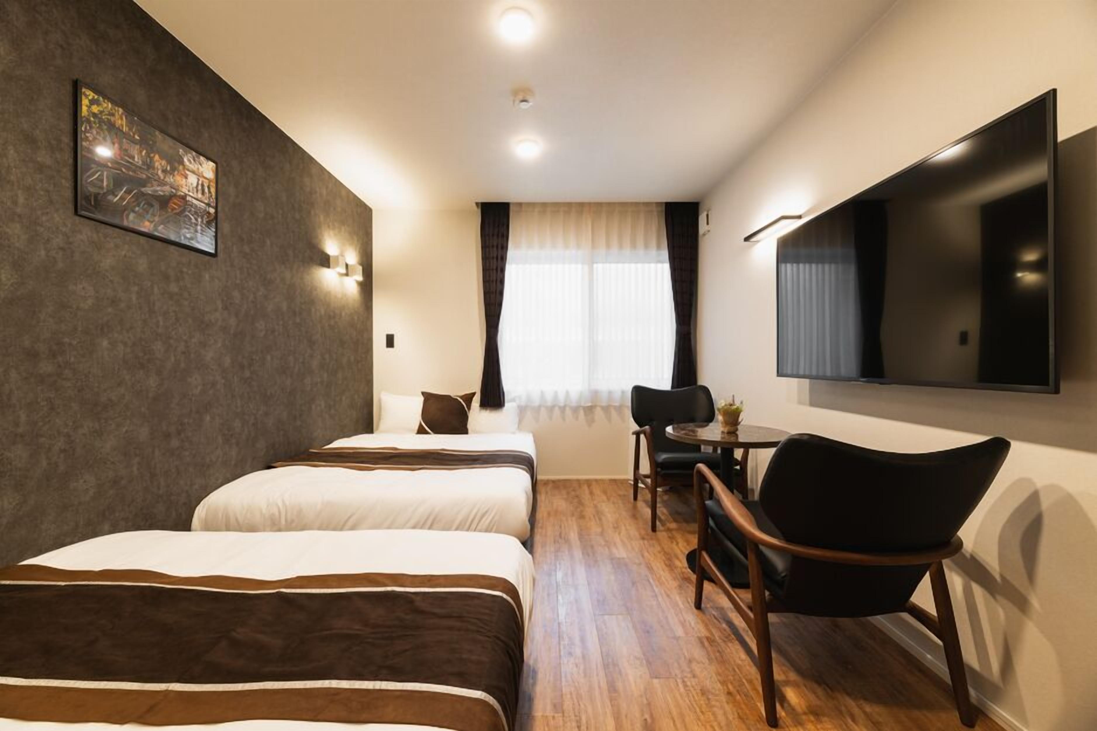A hotel room with two beds, a desk, a chair, a TV, and a window with curtains.