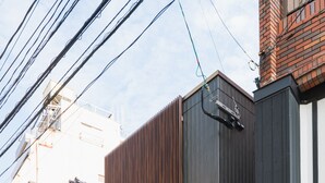 A modern building with a dark facade, a small tree in the front yard, and a visible street sign. - Grand Base Nagasaki (Nagasaki)