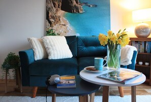 A living room with a dark blue sofa, a white throw pillow, a coffee table with a book and a vase of flowers.