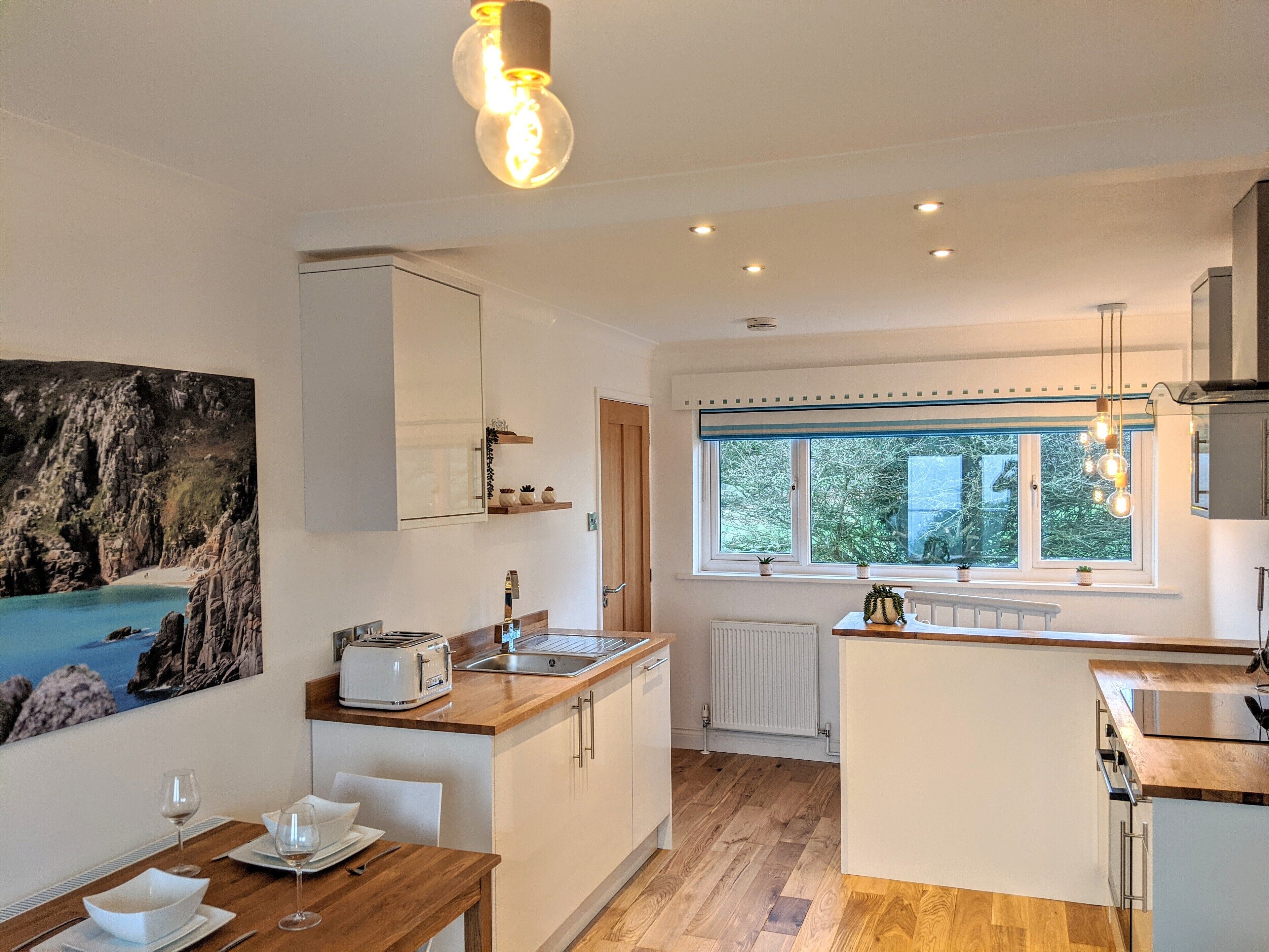 A modern kitchen with white cabinetry, a wooden countertop, a built-in oven, and a window with a view of greenery.