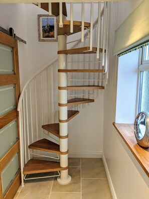 A spiral staircase with wooden steps and white railings, leading to an upper floor.
