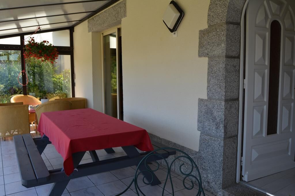 Un patio couvert avec une table pour deux, un banc et une plante suspendue.