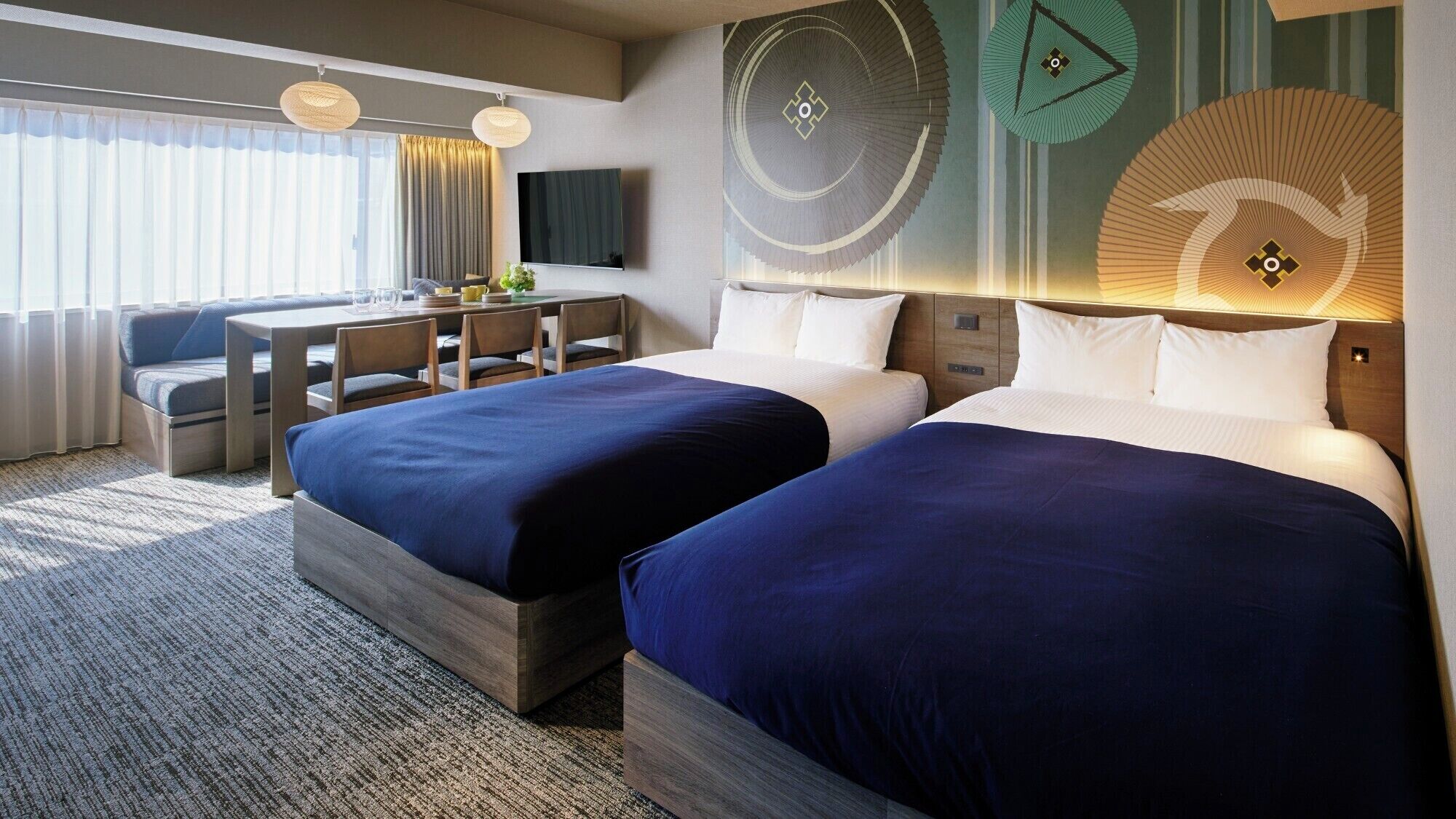 A hotel room with two beds, a desk with chairs, a flat-screen TV, and decorative wall art.