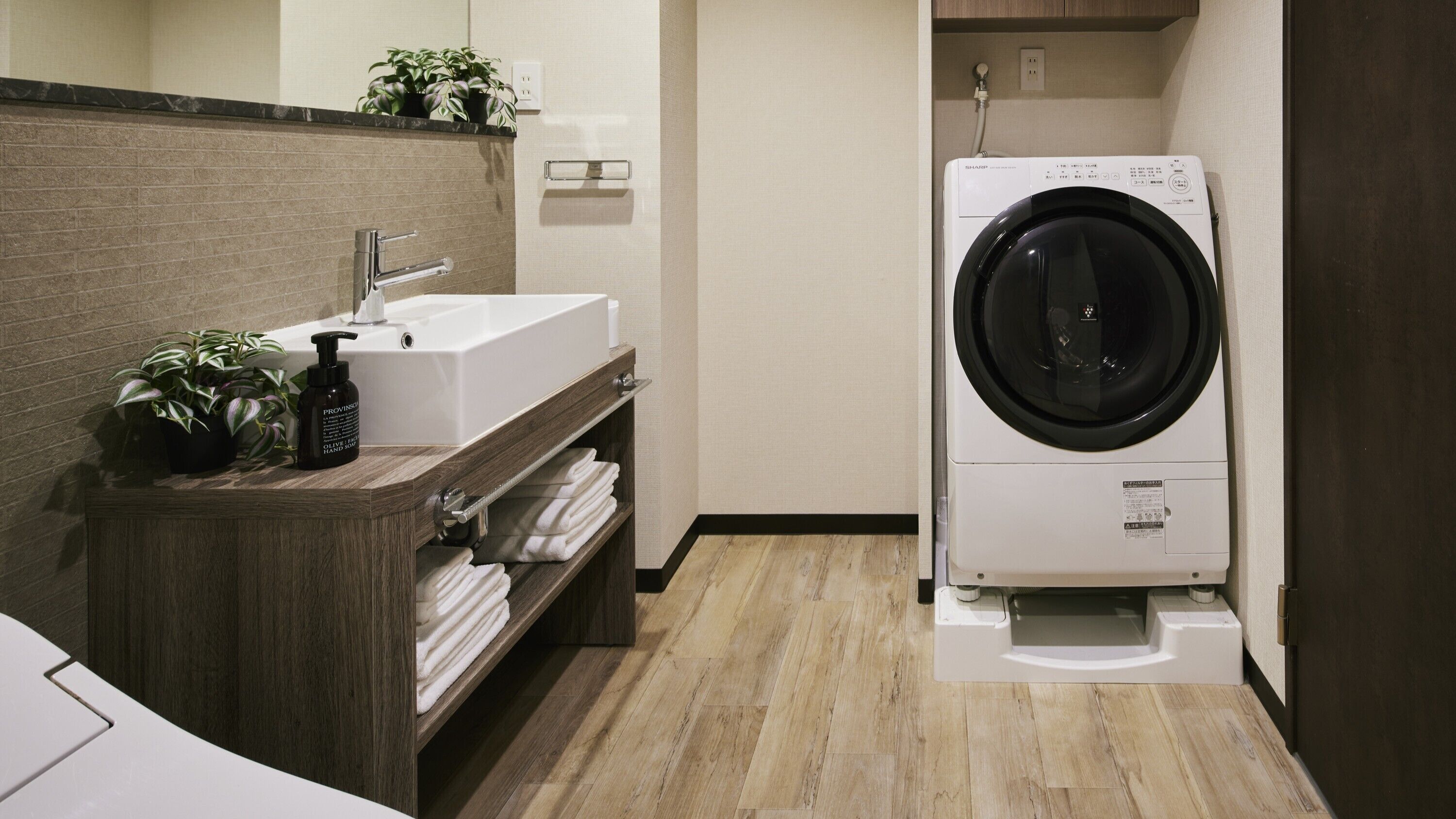 Une petite buanderie équipée d’un lave-linge, d’un évier et d’une étagère où sont pliées les serviettes.