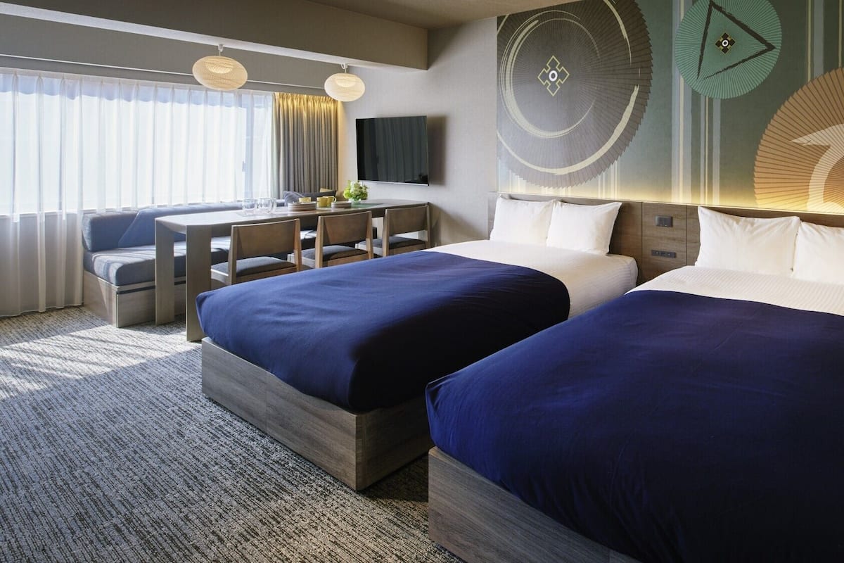 A hotel room with two beds, a desk, and a TV.