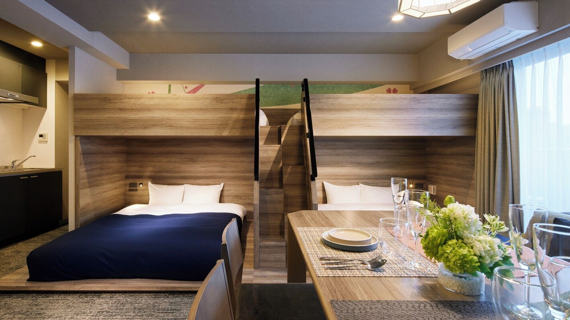 A hotel room with a bunk bed, a dining table set with glasses and cutlery, and a small plant on the table.