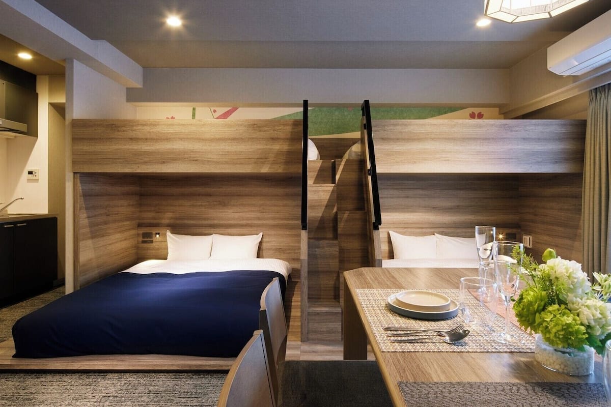 Une chambre d’hôtel avec un lit superposé, une table à manger dressée avec des verres et des couverts, et une petite plante posée sur la table.