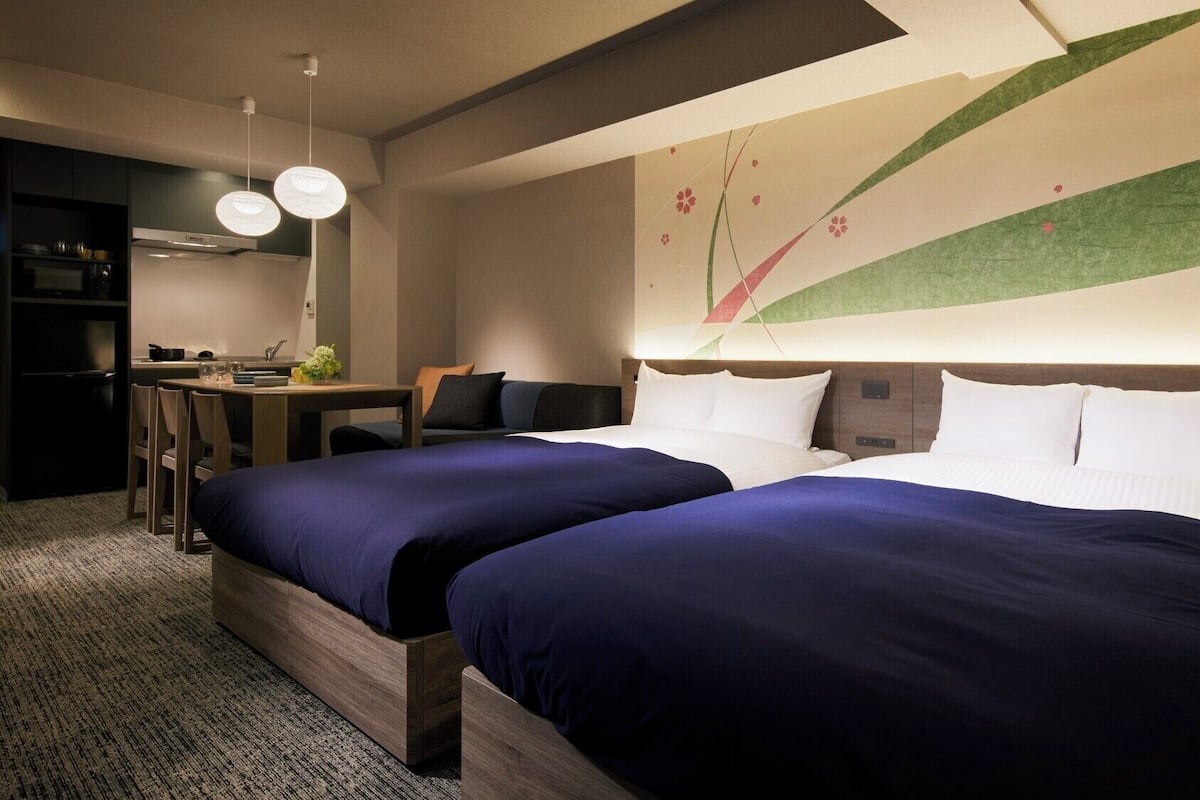 Une chambre d’hôtel avec deux lits, un bureau, une chaise, une petite kitchenette et un mur décoratif.