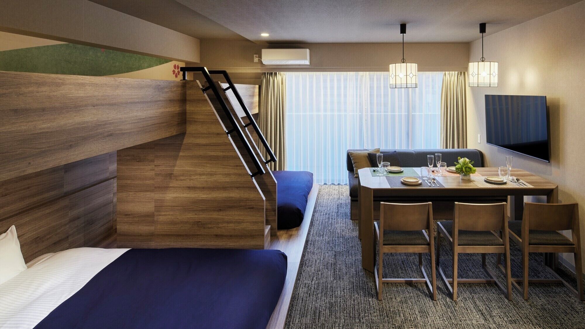 Une chambre d’hôtel avec un lit superposé, un coin repas avec une table et des chaises, un canapé, une télévision et un escalier.