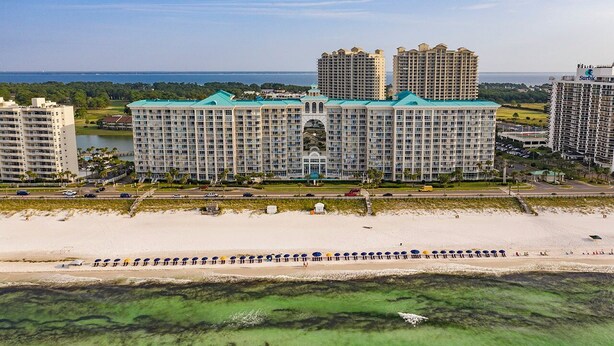 A large hotel with multiple buildings, a beach in the foreground, and a body of water in the background.