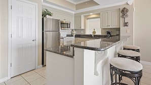 A kitchen with a central island, white cabinetry, stainless steel appliances, and a window with blinds.