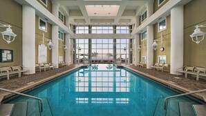 An indoor swimming pool with clear glass walls, white columns, and a tiled floor.