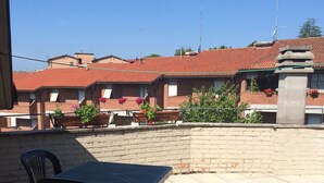An outdoor patio area with a table and chairs, a brick wall, and a view of buildings with red-tiled roofs. - Rinidia Siena Celso Cittadini (Siena)