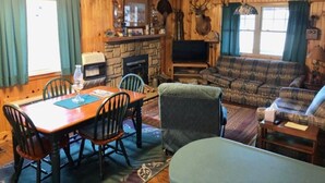 A cozy cabin interior with a stone fireplace, wooden walls, a dining table with chairs, a sofa, and a television. - Workman's Wildlife Haven, Secluded country setting vacation cabin (Louisa)