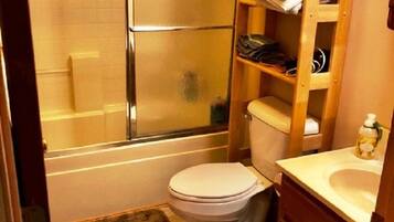 Un bany compacte amb vàter, una estantària de fusta i una cabina de dutxa.