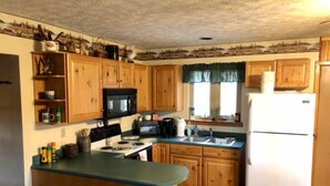 A compact kitchen with wooden cabinets, a microwave, a stove, and a refrigerator. - Workman's Wildlife Haven, Secluded country setting vacation cabin (Louisa)