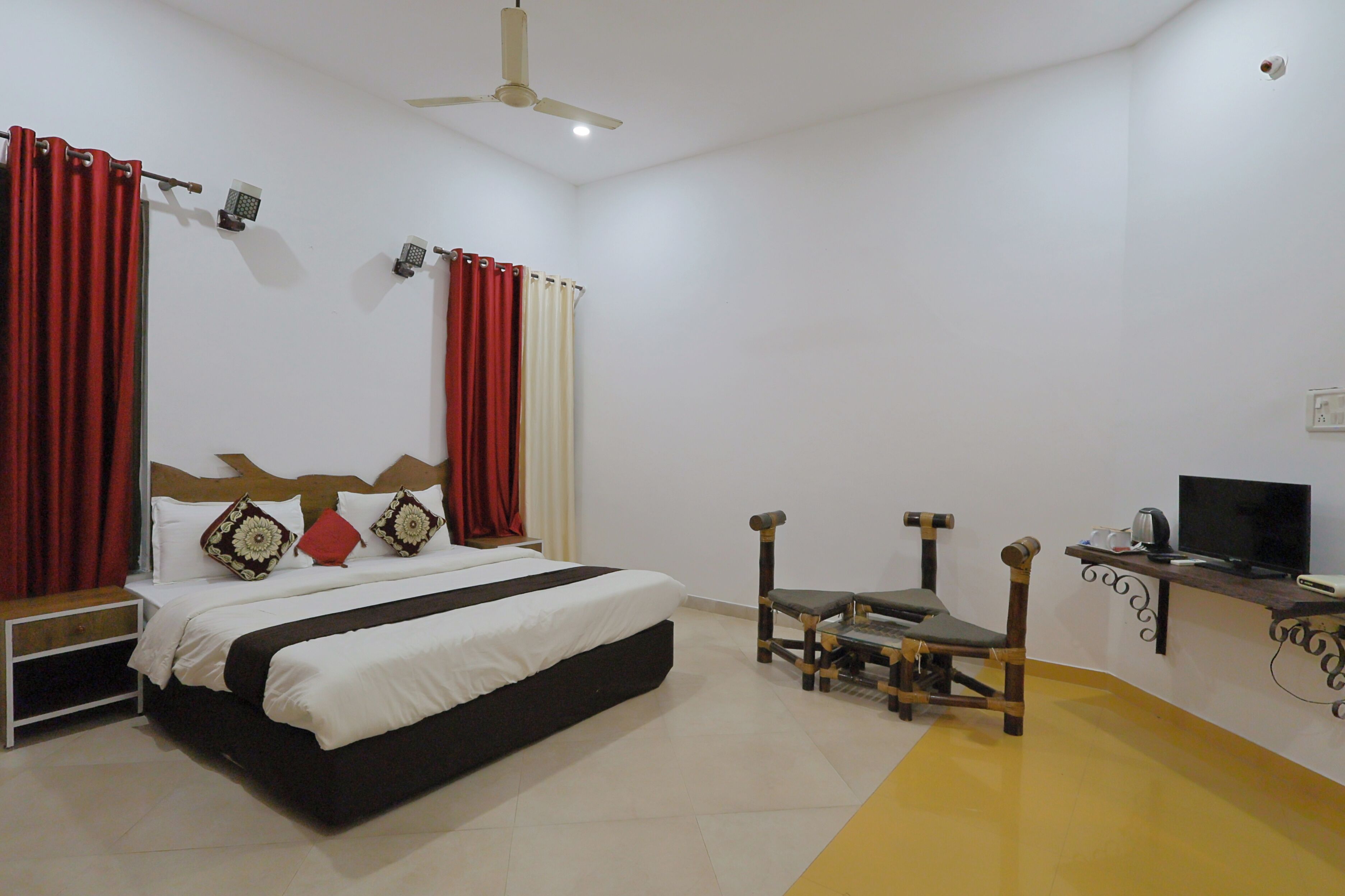 A hotel room with a bed, a desk with a television, a chair, and a ceiling fan.