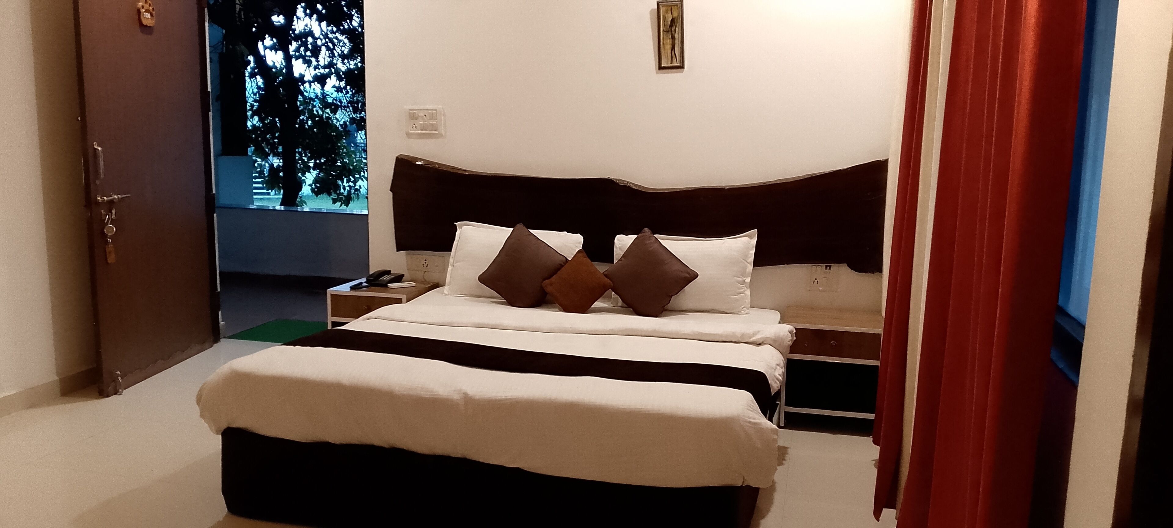 A hotel room with a bed, bedside tables, and a view of a tree through the window.