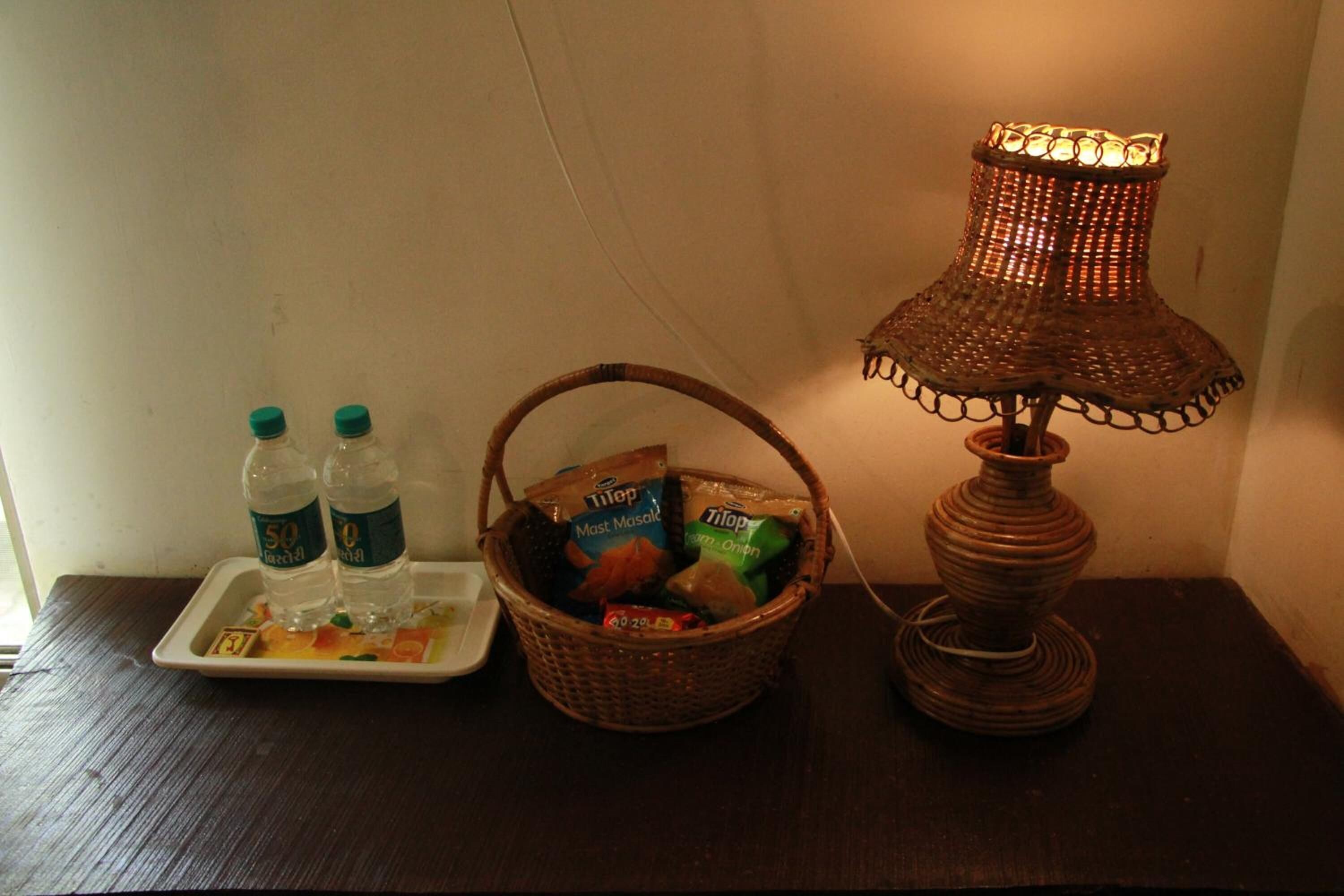 Una mesa con una cesta de alimentos, una bandeja con botellas de agua y una lámpara de mesa.