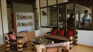 A room with a rattan sofa, a glass coffee table, and a bookshelf. - Nature's Sprout Wildmark Kanha Resort (Bichhiya)