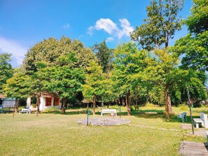 A park with trees, a white building, and a paved area with benches. - Nature's Sprout Wildmark Kanha Resort (Bichhiya)