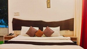 A neatly made bed with a wooden headboard, two bedside tables, and a nightstand with a phone. - Nature's Sprout Wildmark Kanha Resort (Bichhiya)