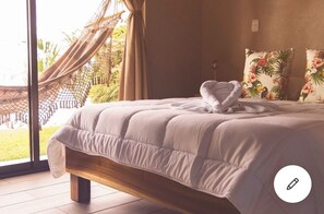 Relax in a serene bedroom with a large bed, quilted headboard, and a view of the outdoors featuring a hammock and lush greenery.