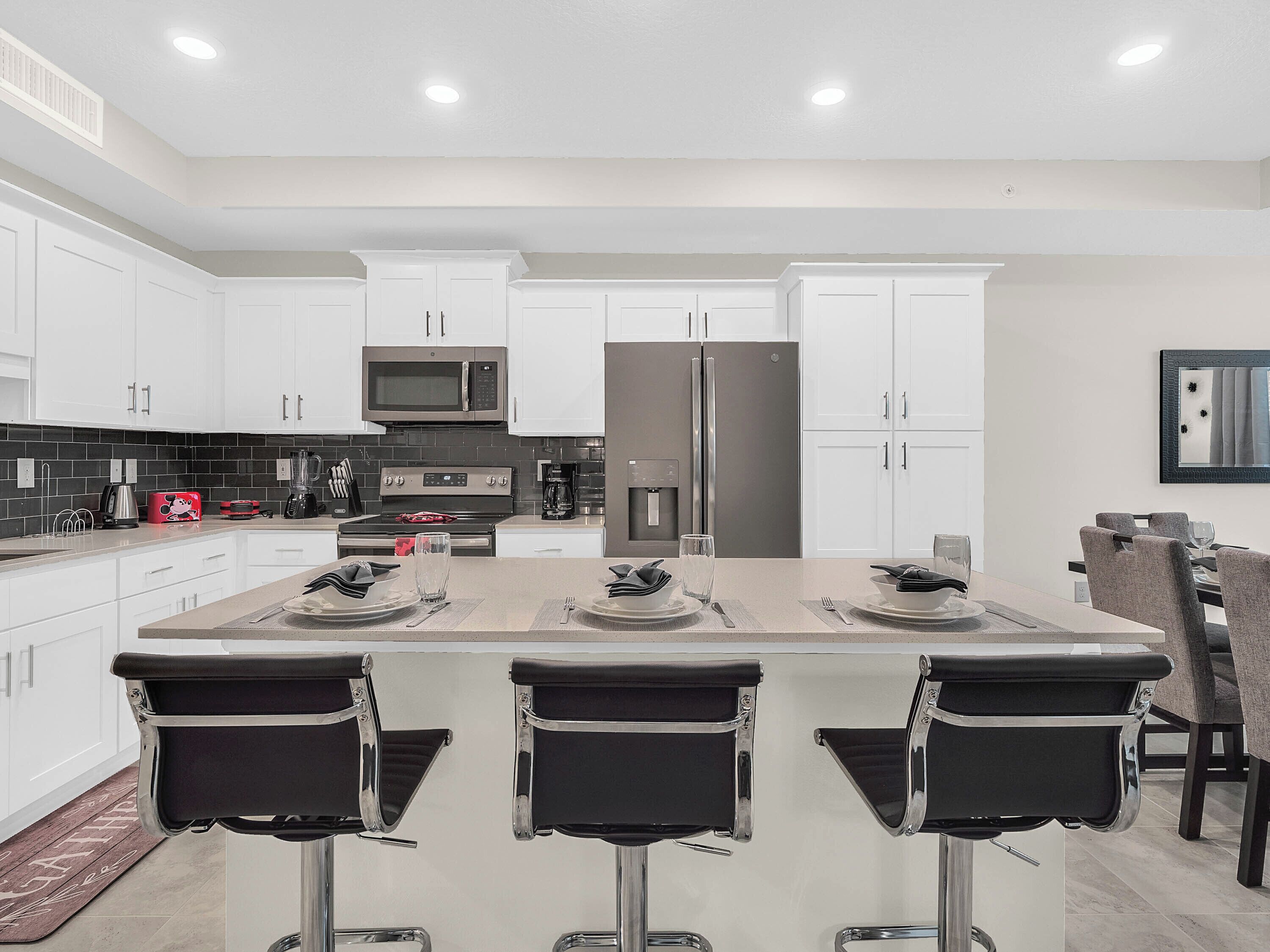 A modern kitchen with white cabinets, stainless steel appliances, and a central island with bar stools.
