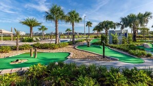 A golf course with multiple green lawns, palm trees, and a clear blue sky.