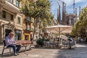 An outdoor café area with tables and chairs, surrounded by buildings with shops and balconies.