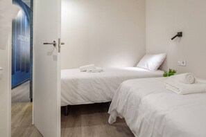 A hotel room with two beds, a door leading to a hallway, and a wall-mounted light fixture.