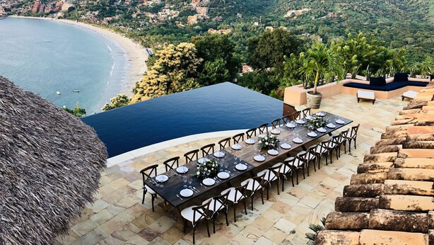 A dining area with a view of a beach and mountains. - Casa Angelina (Zihuatanejo)