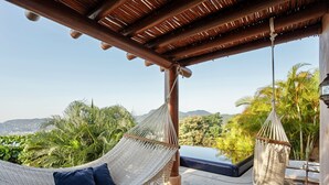 A hammock chair with cushions, a pool, and a view of palm trees and mountains. - Casa Angelina (Zihuatanejo)