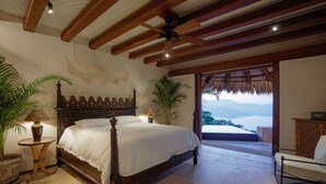 A bedroom with a wooden bed, a nightstand, a lamp, and a view of the mountains through an open door. - Casa Angelina (Zihuatanejo)