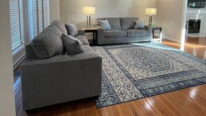 Un salon spacieux avec un grand canapé d’angle gris, un canapé gris plus petit et un tapis à motifs.