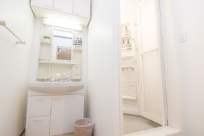 A small, white bathroom with a sink, mirror, and shower. - AMP FLAT Ogokusou (Fukuoka)