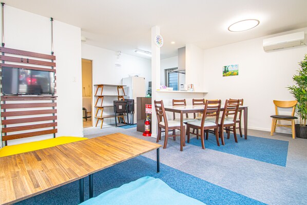 A dining area with a wooden table and chairs, a small kitchen in the background, and a fire extinguisher on the wall. - AMP FLAT Itoshima (Fukuoka)