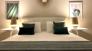 Une chambre d’hôtel bien aménagée, avec un grand lit, deux tables de chevet et deux lampes fixées au mur.