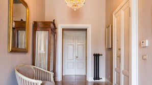 Un couloir avec un lustre, un miroir, un fauteuil à rayures et une porte.
