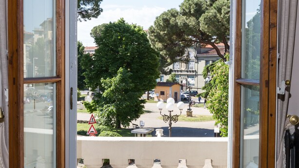 Une porte ouverte donnant sur un balcon avec vue sur une rue, des arbres et des immeubles.