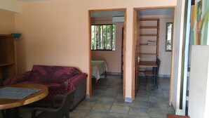 Um quarto com sofá, uma mesa redonda pequena, cama com colcha verde e estante de madeira.