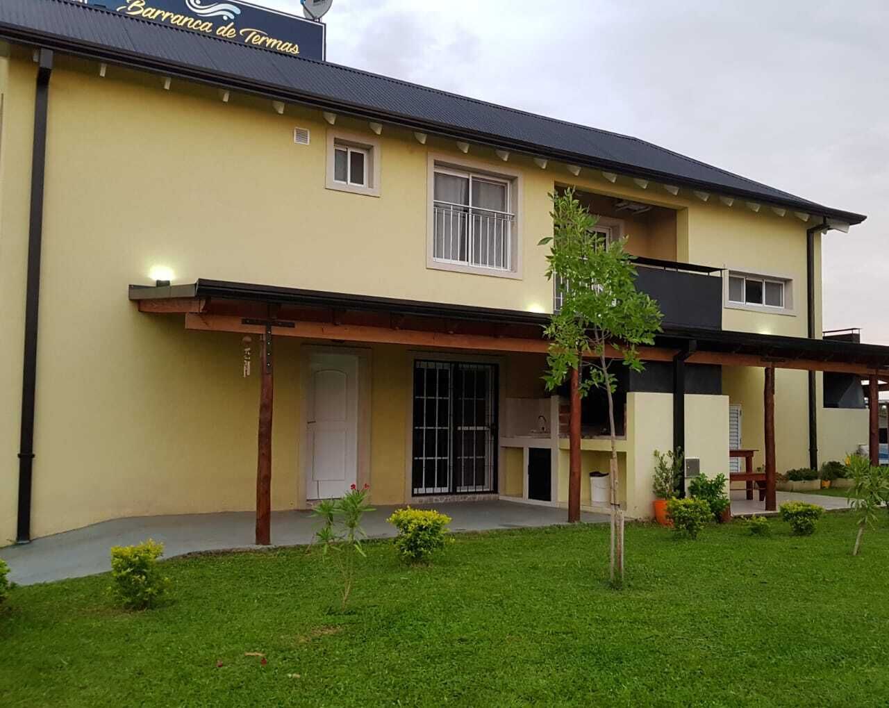 A two-story building with a flat roof, a covered porch, and a small garden area with grass and plants.