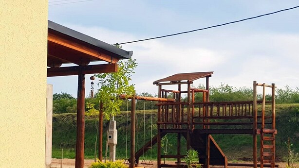 A wooden play structure in a garden with a house in the background.
