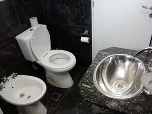 Un baño con inodoro, bidé y lavamanos de acero inoxidable.