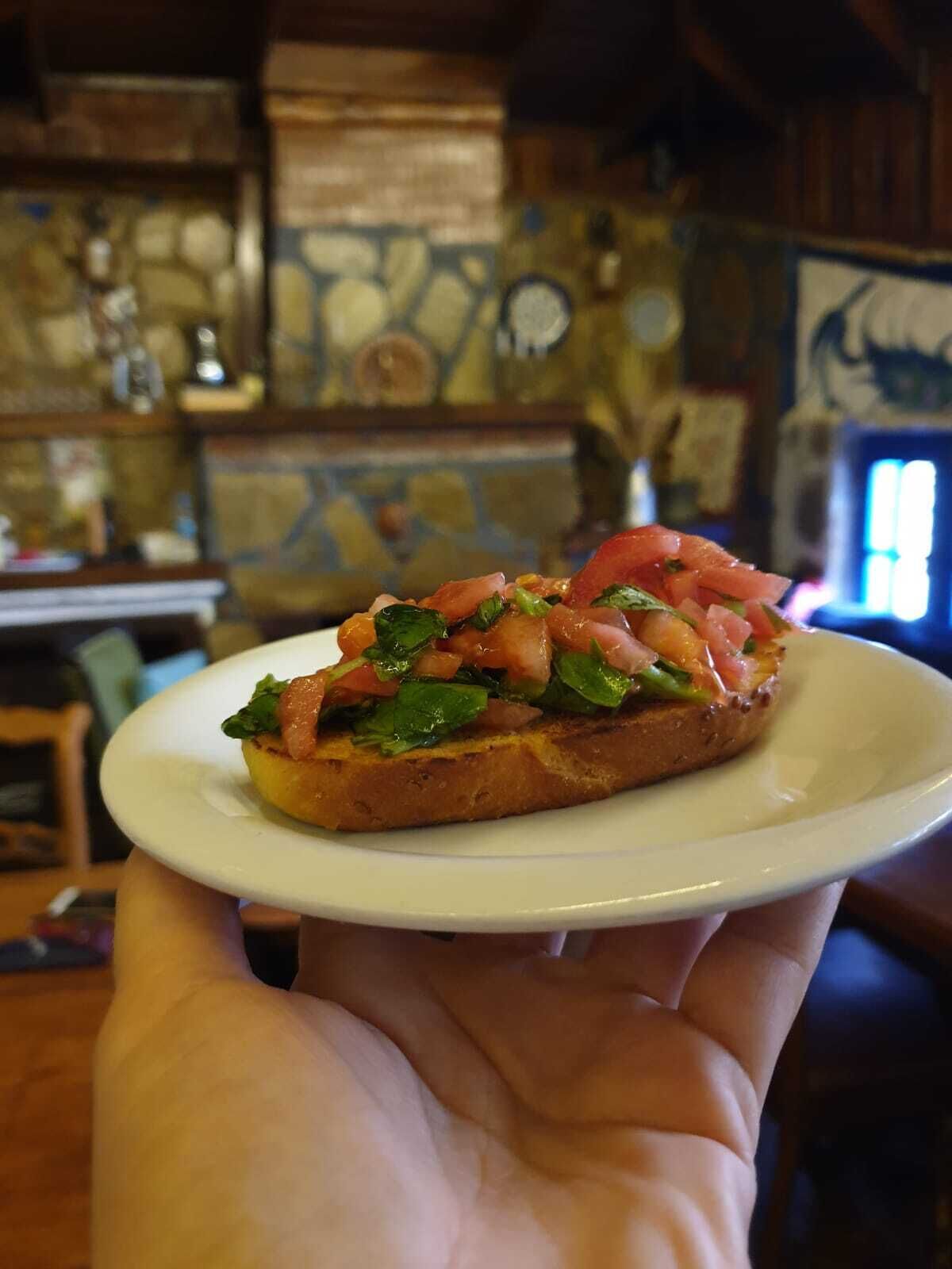Una persona sostiene un plato con un sándwich tostado cubierto de tomate y verduras.
