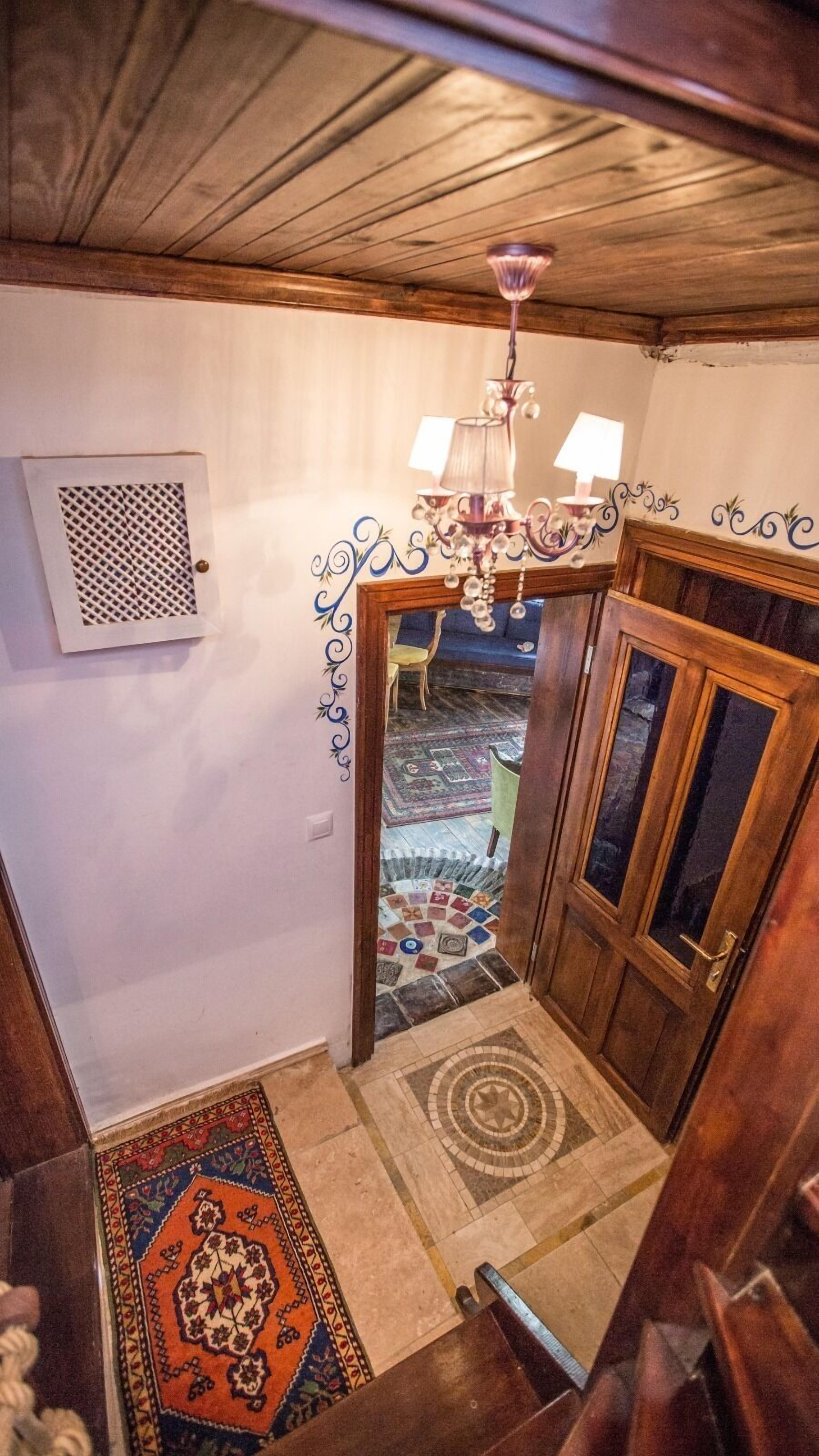 Een houten trap die leidt naar een kamer met een kroonluchter, gekleurde tapijten en decoratieve wanddecoratie.