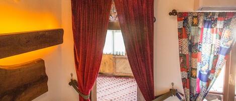 Un dormitorio con cabecera de madera, araña, cortinas rojas y cama con toalla blanca.